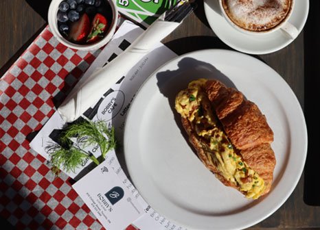 Croissant breakfast sandwich with coffee and fresh berries at Bobby's Breakfast Cafe & Bar in Toronto